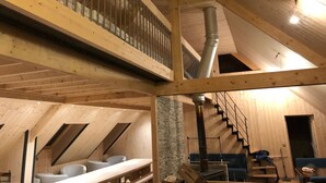 A wooden interior with a loft bedroom, a staircase, and a fireplace.