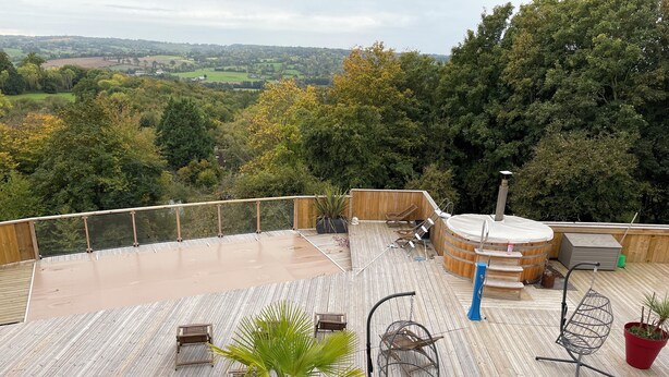 A wooden deck with outdoor seating, a hot tub, and a view of the countryside.