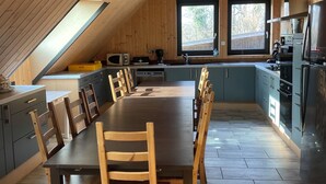A modern kitchen with a large dining table, wooden chairs, and a built-in oven.