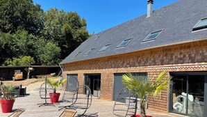 A wooden deck with lounge chairs and potted plants, a brick building with large windows, and a clear blue sky.