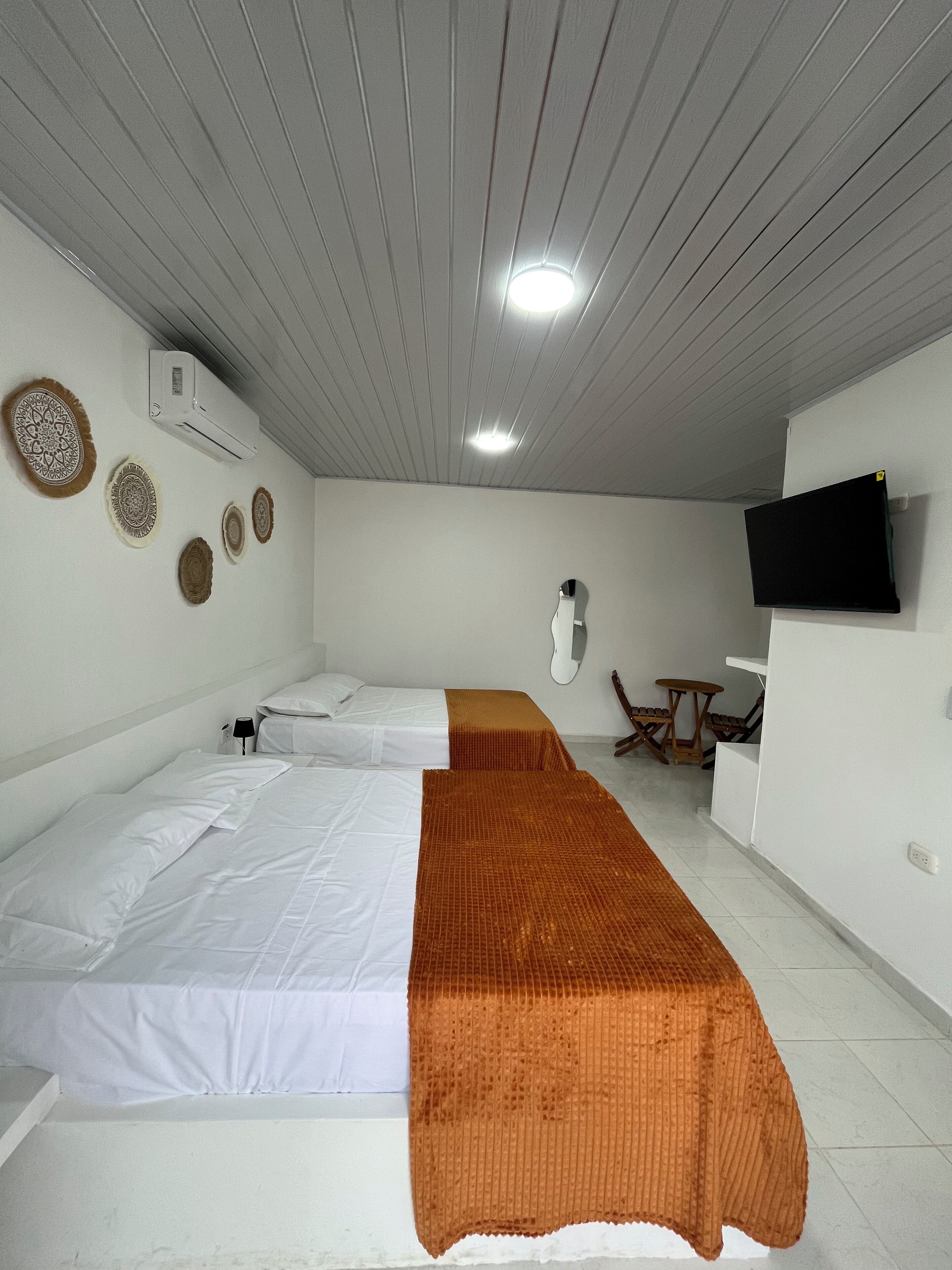 Quarto de hotel com duas camas, televisão, uma mesinha e painéis decorativos na parede.