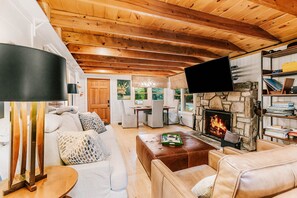 A cozy living room with a stone fireplace, a television mounted on the wall, and a bookshelf filled with books.