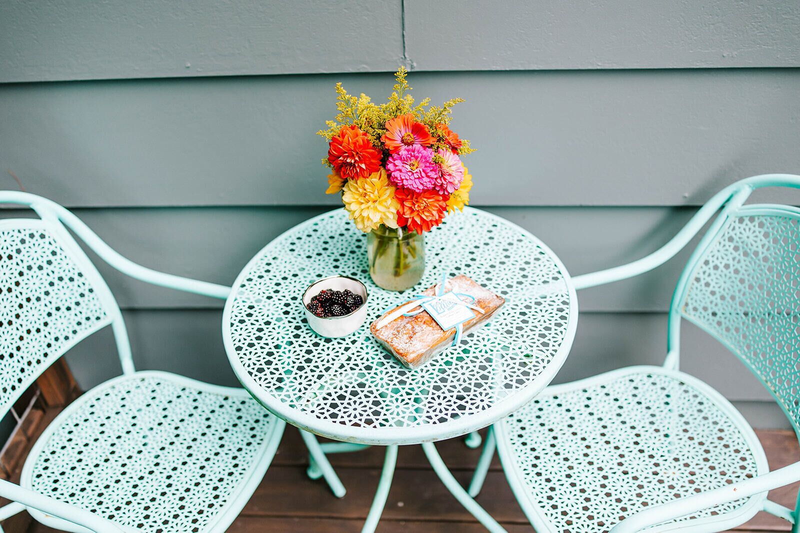 A round table with a vase of flowers, a bowl of berries, and a wrapped gift on a metal chair.