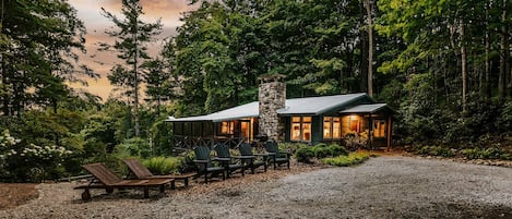 A cabin with a stone chimney, wooden deck, and outdoor seating.