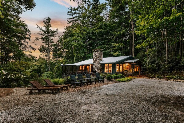 A cabin with a stone chimney, wooden deck, and outdoor seating.
