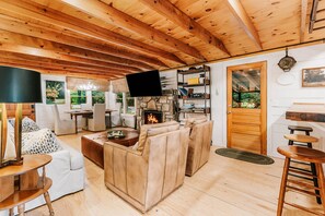 A cozy living room with a fireplace, wooden ceiling, and a television. - New Listing! Mountain Views - Fire pit - Walk to downtown Cashiers (Cashiers)