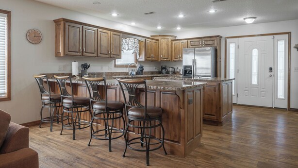 Una cocina amplia con armarios de madera, una isla central con taburetes de bar y un refrigerador empotrado.
