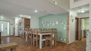 Un comedor amplio con una mesa y sillas de madera, una cocina con armarios de madera, y una pared decorada con cuadros enmarcados.