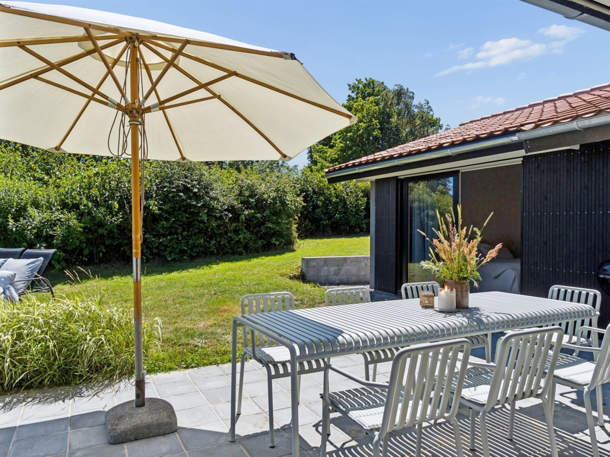 An outdoor patio with a table and chairs, a large umbrella, and a modern building in the background.
