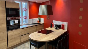 A modern kitchen with wooden cabinets, a built-in oven, a microwave, and a red accent wall.