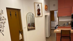 Een moderne woonkamer met een gele bank, een houten eettafel en een keuken met roze kastjes.