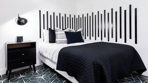 Una camera da letto moderna con una testiera a righe bianche e nere, un comodino nero con cassetti e un pavimento con motivo geometrico.