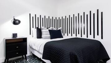 A modern bedroom with a black and white striped headboard, a black bedside table with drawers, and a geometric patterned floor.