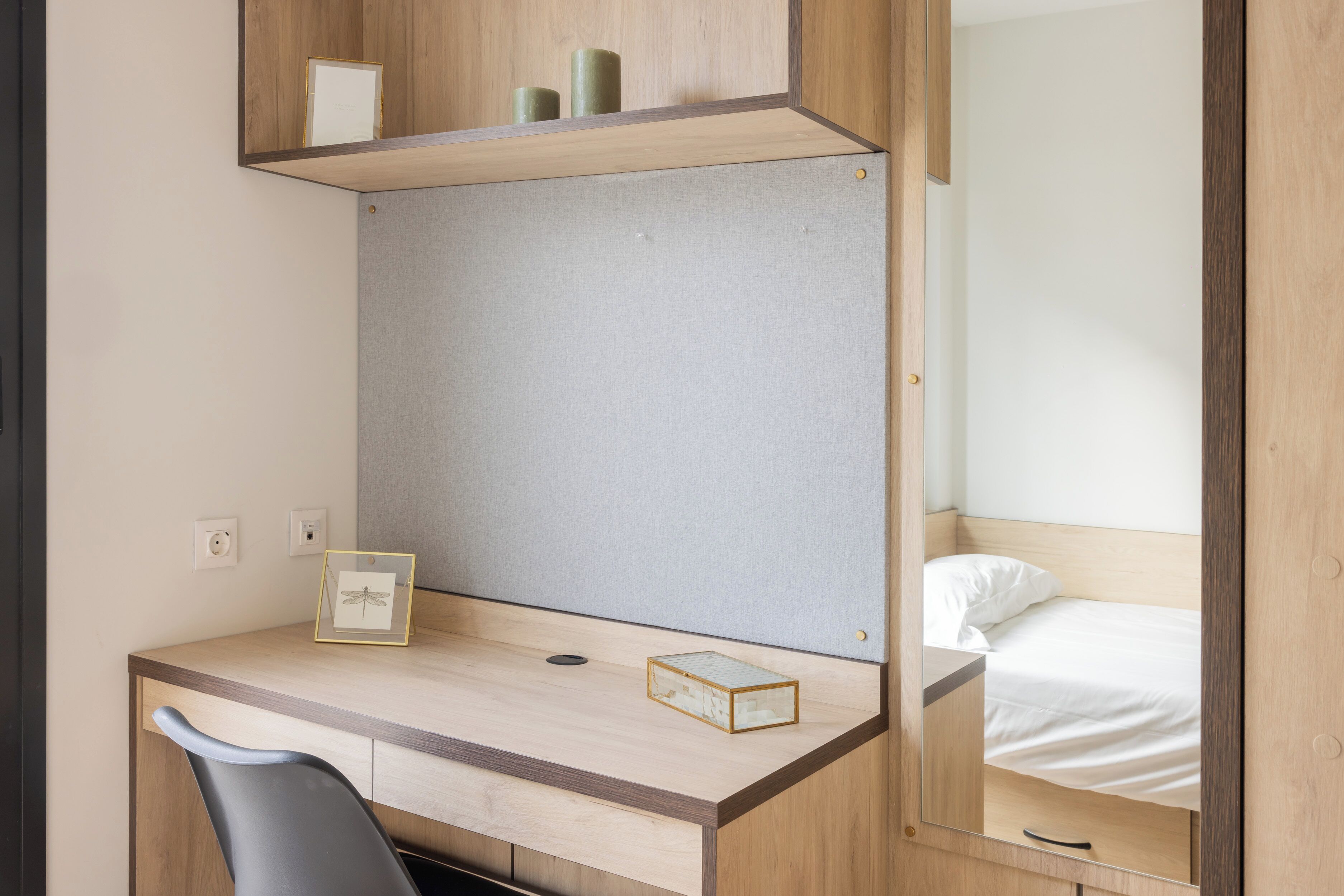 A compact bedroom with a wooden desk, a single bed, and a mirror.