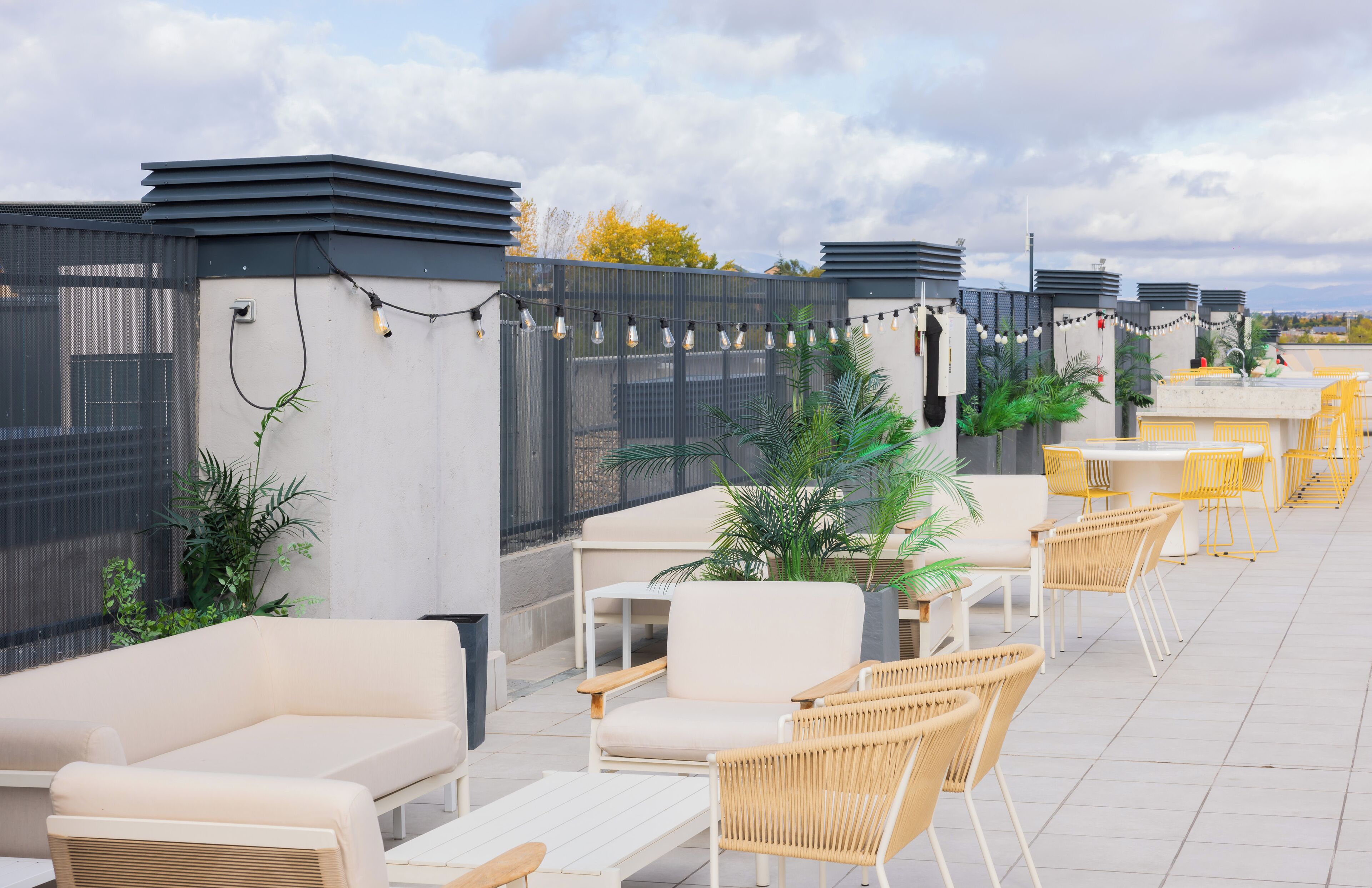 Una terraza en la azotea con mobiliario exterior, plantas en macetas y guirnaldas de luces.