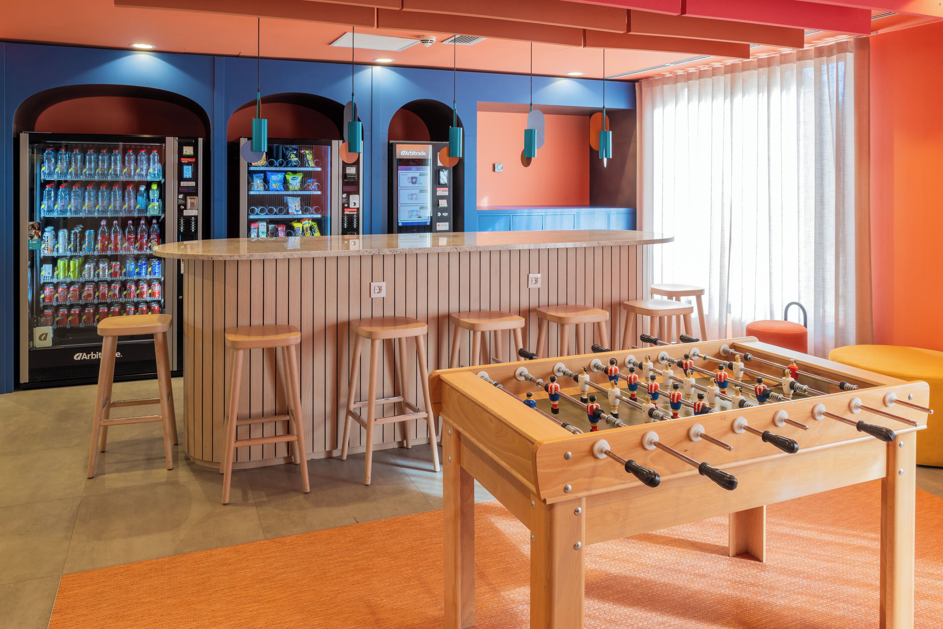 Una habitación con mesa de fútbol, zona de bar con taburetes y máquinas expendedoras.