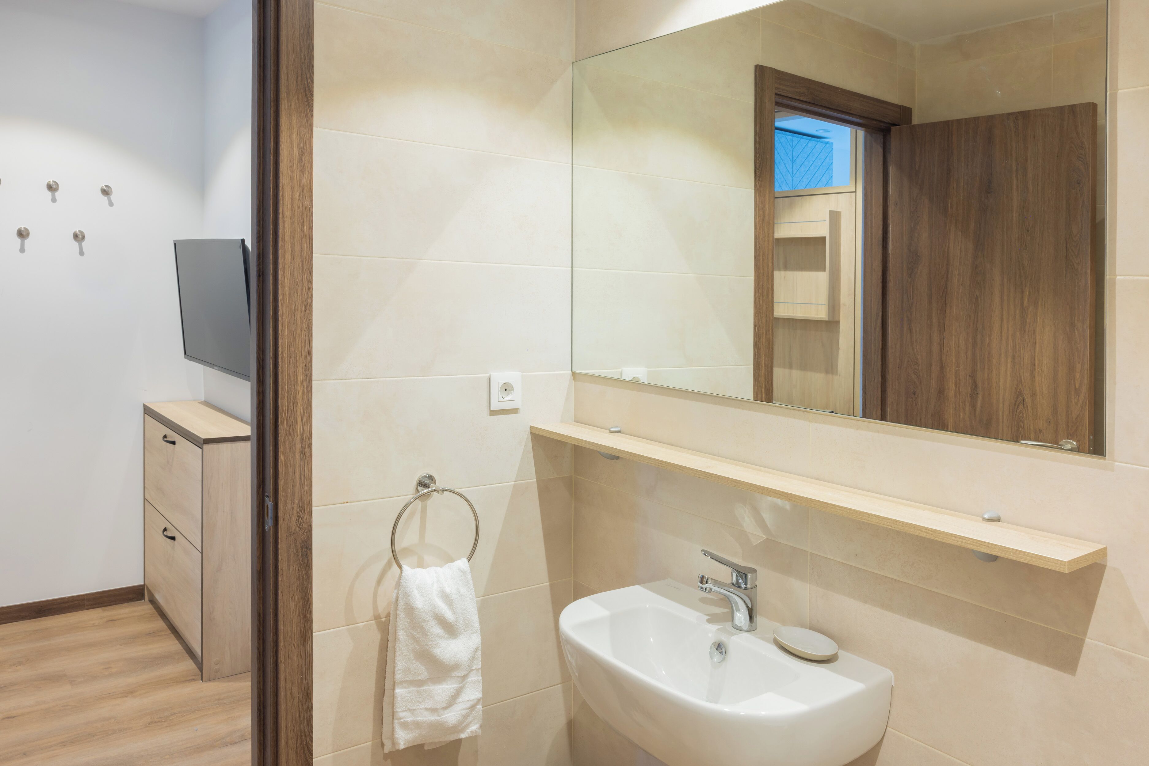 A modern bathroom with a wooden cabinet, a white sink, and a mirror above it.