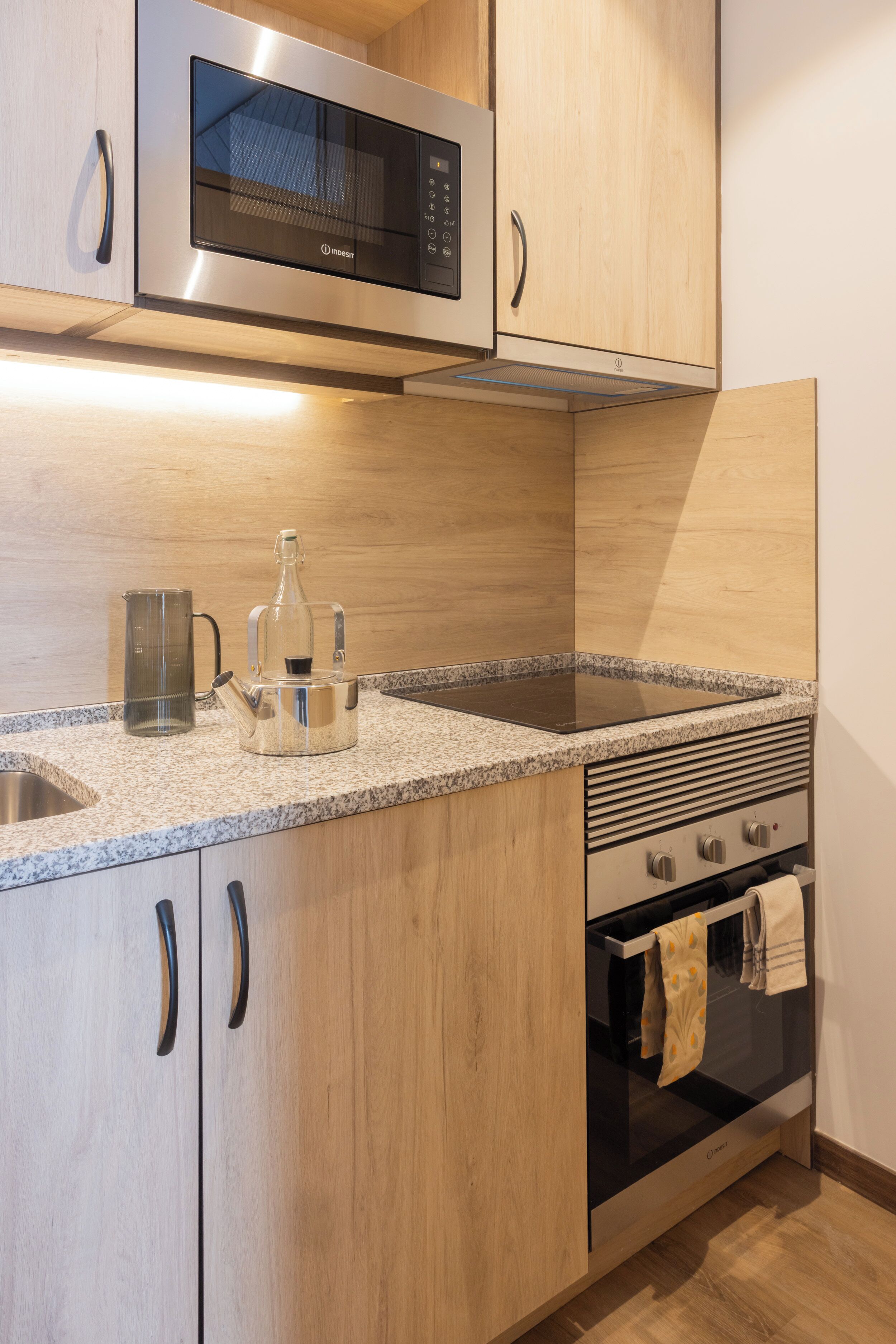 A modern kitchen with stainless steel appliances, granite countertops, wooden cabinets, and a built-in oven.