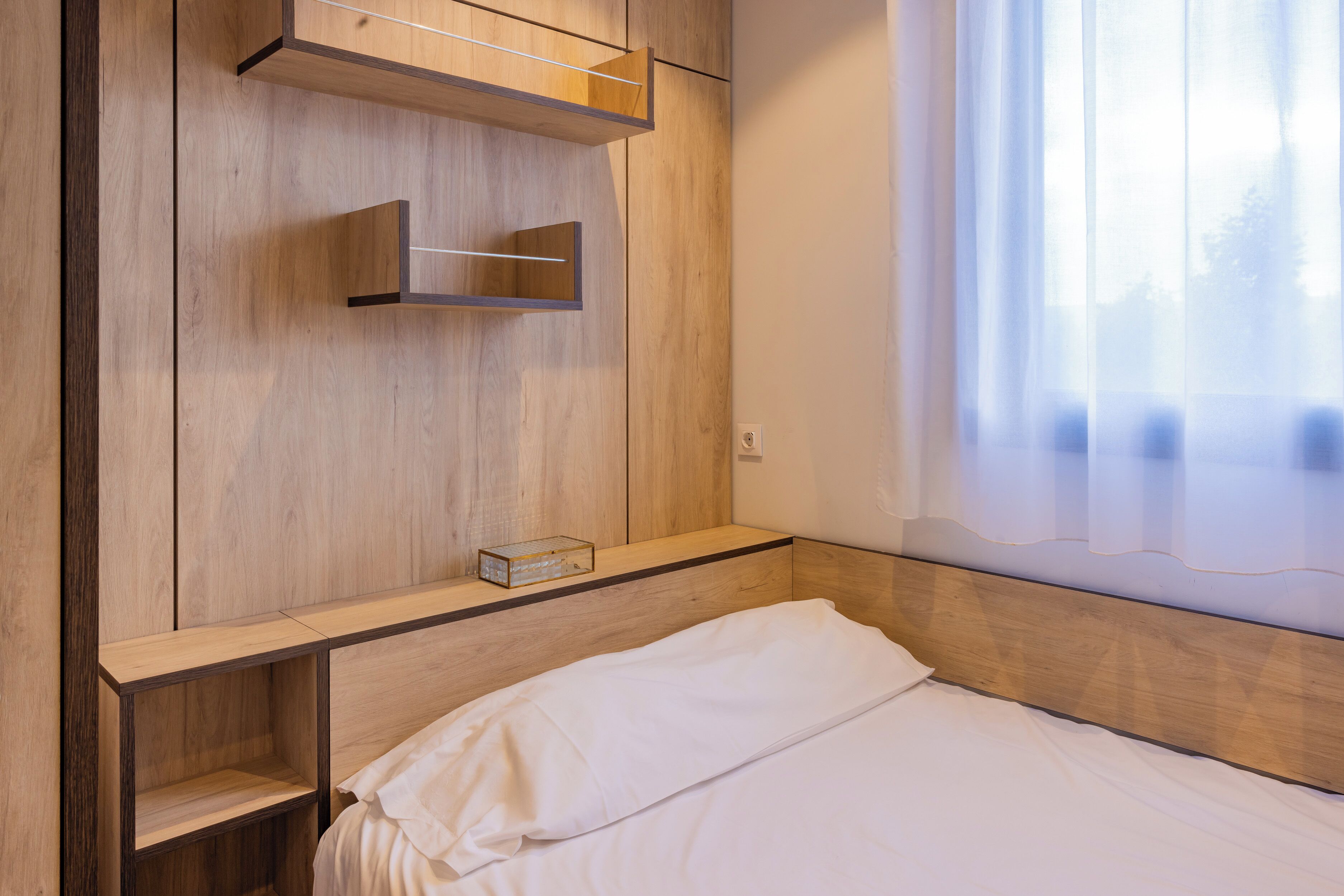 A bedroom with a wooden headboard, a bed with white bedding, and built-in shelves.