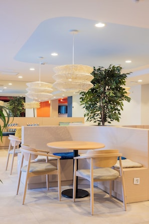 Een modern zithoek met ronde tafels en stoelen, een grote kamerplant en opvallende hanglampen.