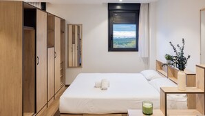 Een slaapkamer met een bed, een kledingkast, een raam met uitzicht en een nachtkastje met een vaas.