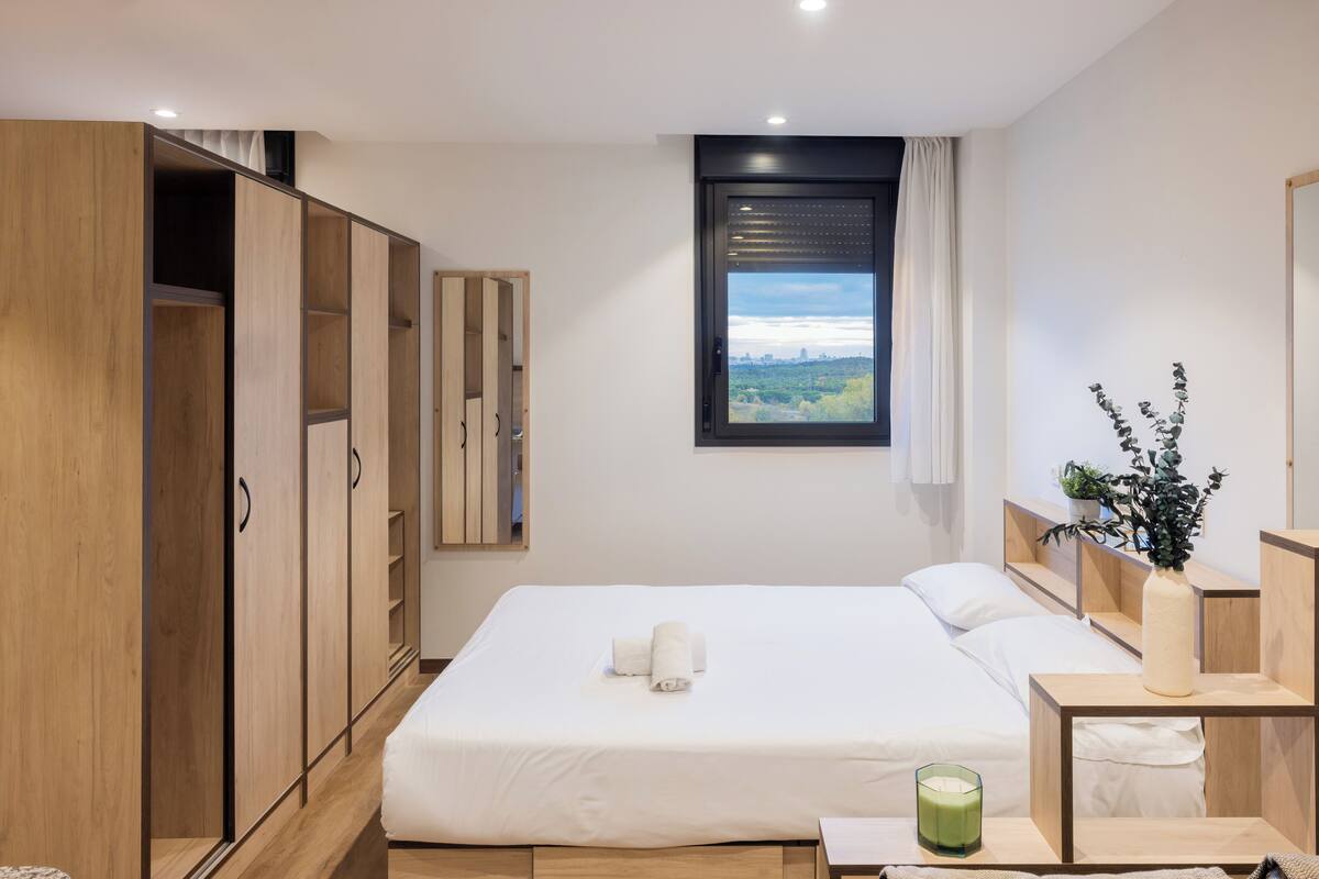 Een slaapkamer met een bed, een kledingkast, een raam met uitzicht en een nachtkastje met een vaas.