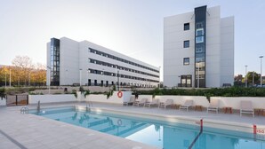 Een modern gebouw met een zwembad, ligbedden en een reddingsboei.