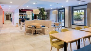 Een moderne eetruimte met houten tafels en stoelen, een receptiebalie en grote ramen met uitzicht op de omgeving.