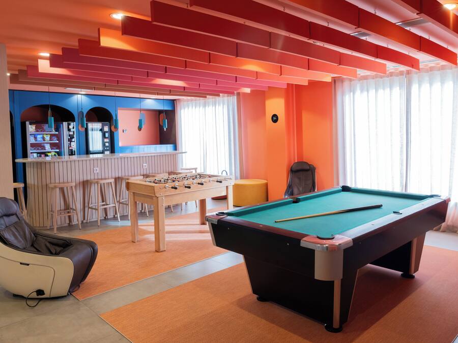 Una mesa de billar, un sillón de masaje y una mesa de futbolín en una habitación con paredes anaranjadas y una zona de bar.