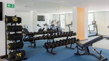 A gym with exercise equipment, dumbbells, and a bench.