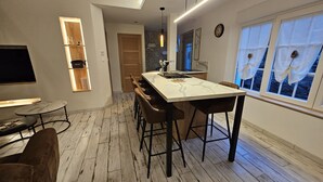 Eine moderne Küche mit Marmorarbeitsplatte, Holzstühlen und integriertem Fernseher.