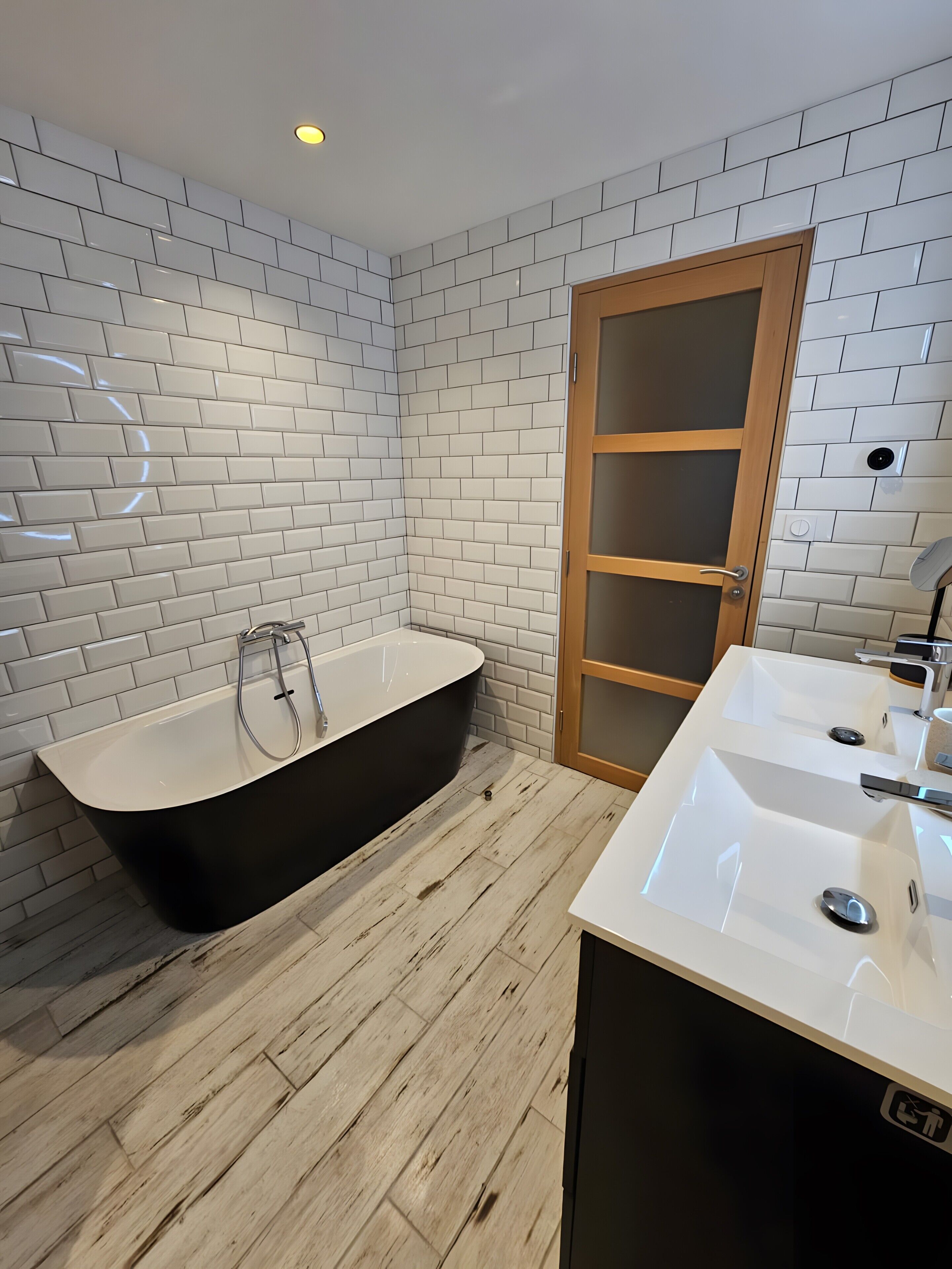 A bathroom with a black freestanding bathtub, a white sink with a mirror, and a wooden door with a frosted glass panel.
