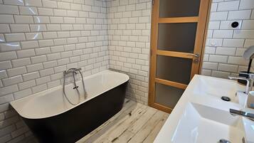 A bathroom with a black freestanding bathtub, a white sink with a mirror, and a wooden door with a frosted glass panel.