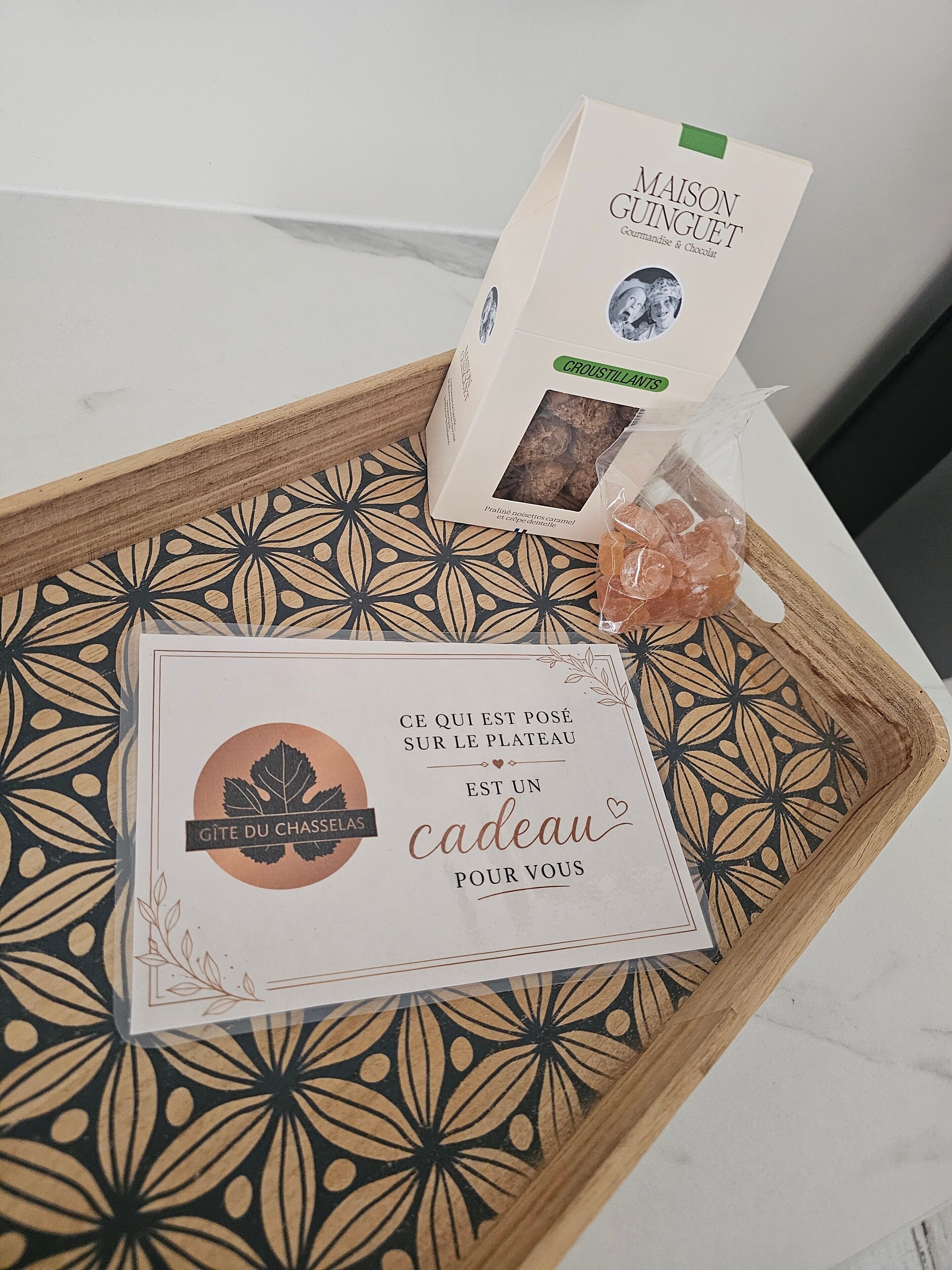 A tray with a box of Maison Guinguet chocolate, a bag of croissants, and a card with a gift message.