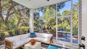 A covered patio with a white sofa, blue cushions, and a wooden coffee table. - Seafarer Lodge - 2 properties - one roof one price! (Jekyll Island)