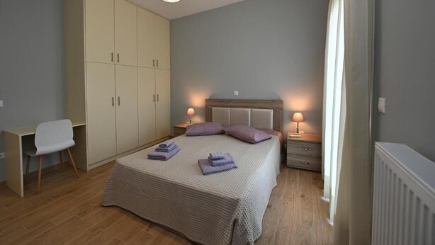 Ein Schlafzimmer mit Bett, Nachttischen, einem Kleiderschrank, einem Sessel und einer Pendelleuchte.