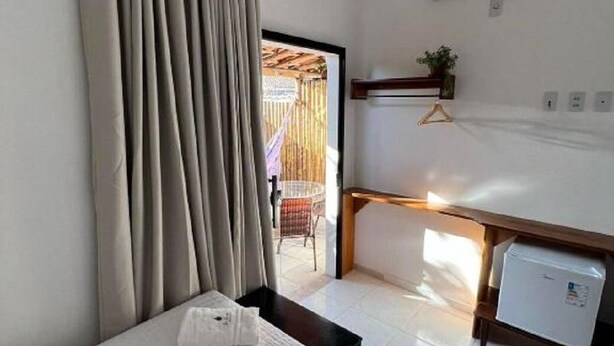A hotel room with a bed, a desk, a small refrigerator, an air conditioner, and a view of the outside. - La Fluorita Hospedaria (Morro Do Chapeu)