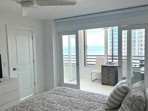 Ein Schlafzimmer mit einem Bett, einem Schreibtisch, einem Sessel und Blick auf den Ozean durch große Fenster.