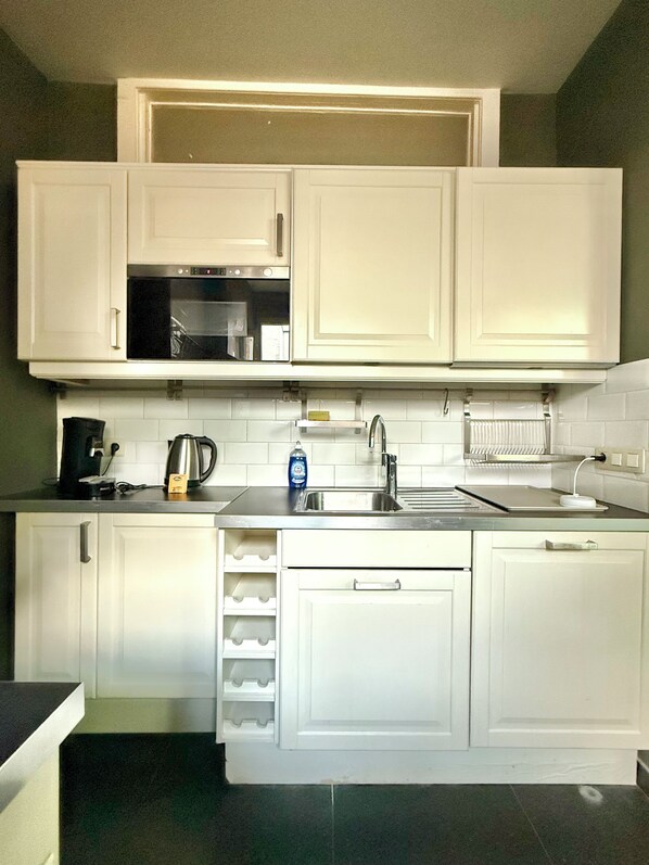 Cocina moderna con gabinetes blancos, un lavamanos de acero inoxidable y un horno empotrado.