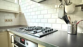 A kitchen with a gas stove, oven, and a hanging pot rack.