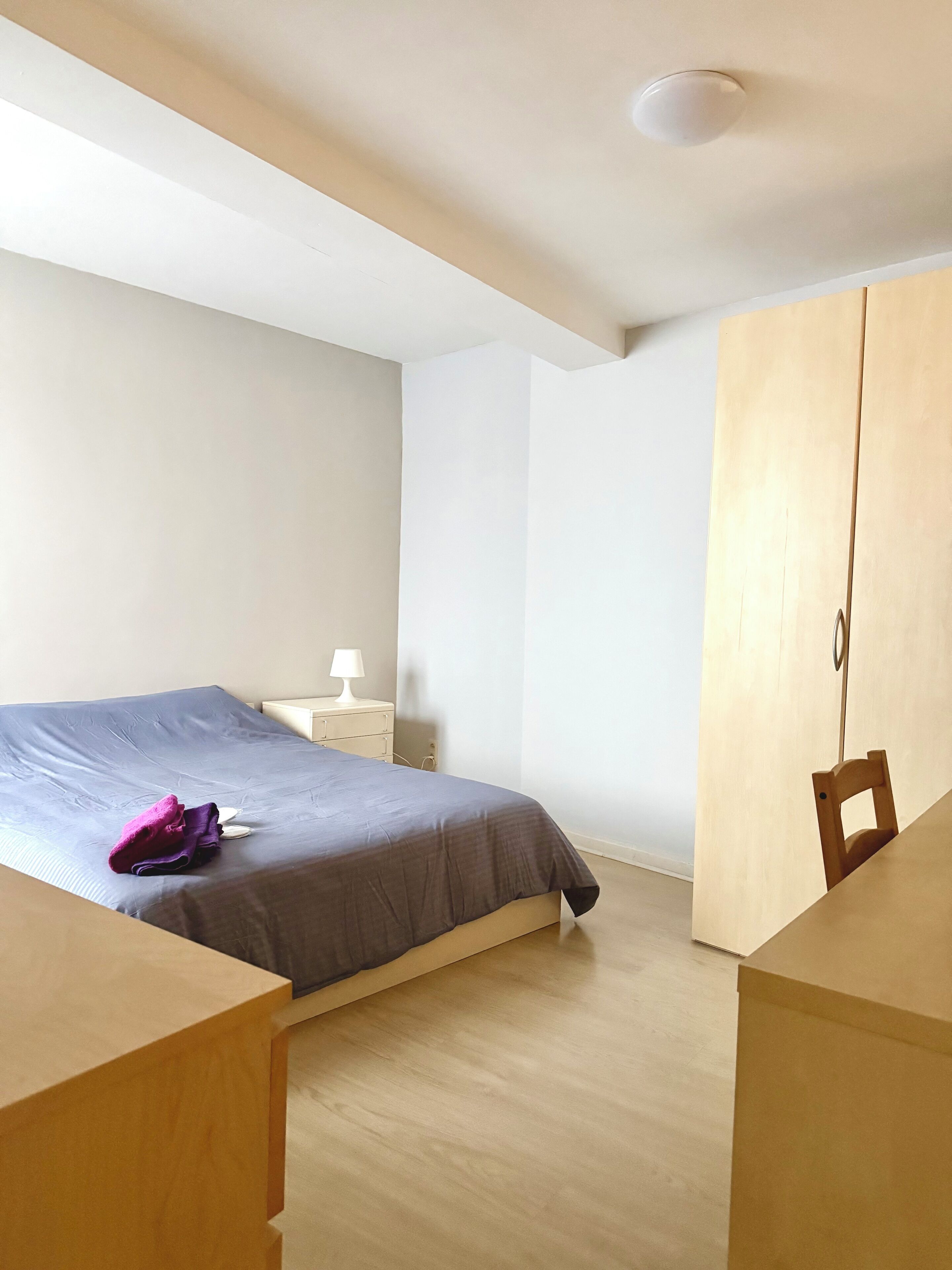 Un dormitorio con cama, mesita de noche, lámpara y armario de madera.