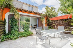 A patio with a table and chairs, a covered seating area, and a building with a sliding glass door. - Gîte Navacelles (Lavérune)