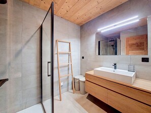 A modern bathroom with a glass shower door, a wooden ladder, a large mirror, and a wooden vanity with a sink.