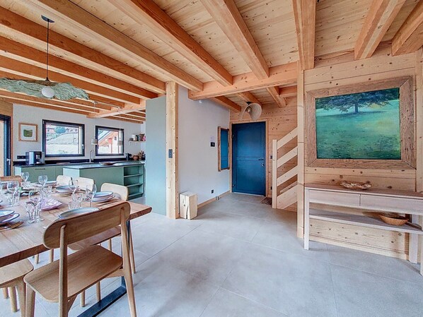 A wooden interior with a dining area, kitchen, and a large window with a painting.