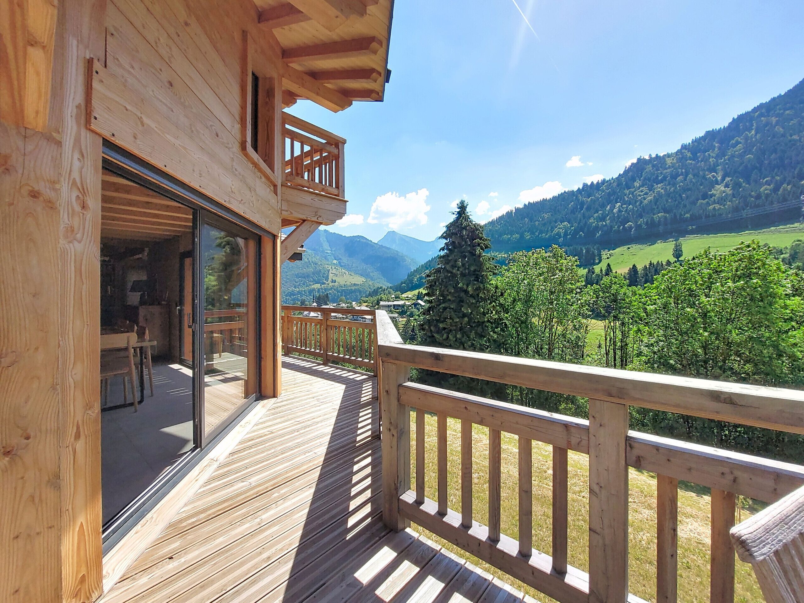 Una terraza de madera con una puerta de vidrio que da a una habitación, con vistas a un paisaje montañoso.