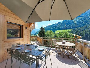 Eine Holzterrasse mit Tisch und Stühlen, einem großen Sonnenschirm und Blick auf eine reizvolle Berglandschaft.