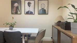 Un comedor con una mesa, sillas, una planta en maceta y cuadros en la pared.
