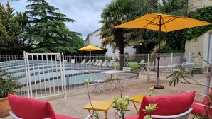 A poolside area with white metal chairs and tables, a yellow umbrella, and a pool with a white fence. - La Villa Richelieu (Châtellerault)