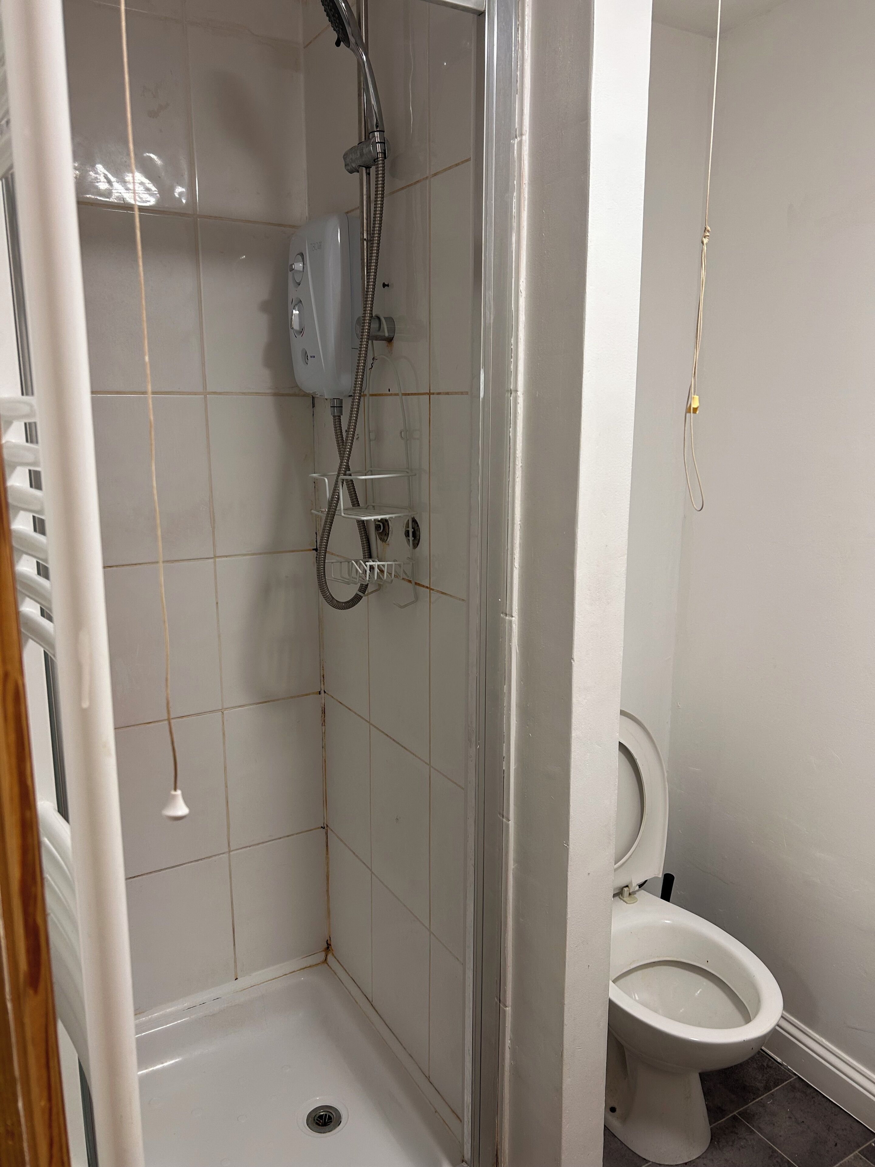 A small bathroom with a shower, toilet, and a towel rack.