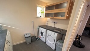 A compact laundry room with a washing machine, a dryer, a trash bin, and a mop.